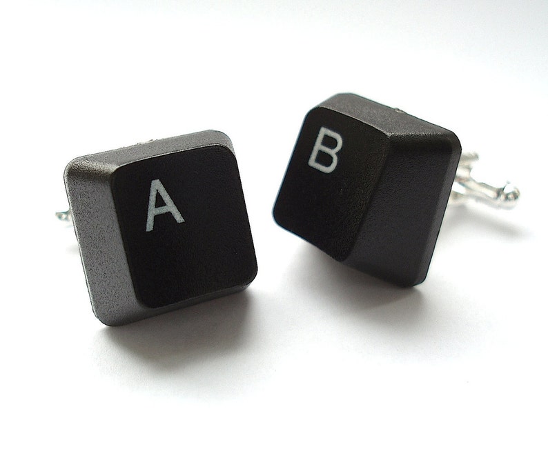 May include: A pair of black cufflinks shaped like computer keys. The keys are labeled "A" and "B" in white.