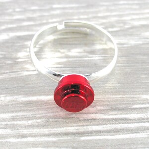May include: A silver adjustable ring with a red LEGO brick as the centerpiece. The brick has the LEGO logo in white.