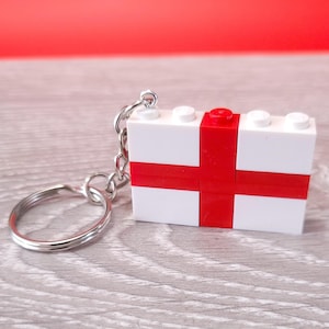 May include: A white and red Lego keychain shaped like the flag of England. The keychain has a silver ring and chain.