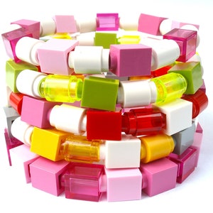 Può includere: Un braccialetto colorato fatto di mattoncini Lego in rosa, bianco, giallo, verde, rosso e grigio.