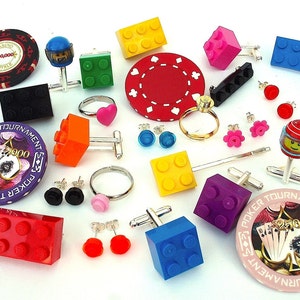 May include: A collection of colorful Lego cufflinks, earrings, and rings. The cufflinks feature various Lego bricks, including red, blue, yellow, and purple. The earrings are small and feature Lego bricks in various colors. The rings are gold and feature a Lego brick design. The image also includes a poker chip with the text "Casino Royale 100,000".