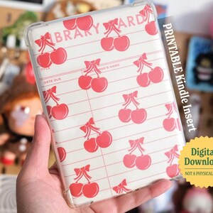 May include: A clear plastic case with a printable design for a Kindle e-reader. The design features a white background with red cherries and the text "LIBRARY CARD".