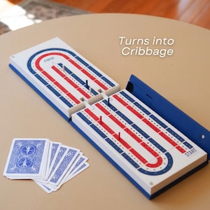 May include: A cribbage board game in blue, red, and white. The board is open, with pegs inserted, and a deck of playing cards is visible. The text "Turns into Cribbage" is in the image.