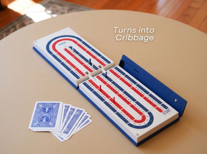 May include: A cribbage board game in blue, red, and white. The board is open, with pegs inserted, and a deck of playing cards is visible. The text "Turns into Cribbage" is in the image.