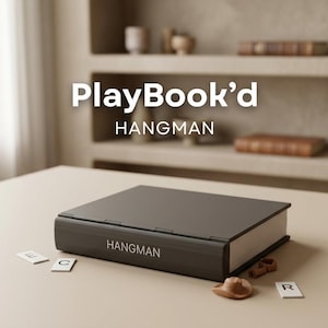 Puede incluir: Un juego Hangman PlayBook'd gris oscuro sobre una superficie beige claro. El juego cerrado, parece un libro, con la palabra "HANGMAN" impresa en el lateral. Hay letras y un sombrero pequeño esparcidos.