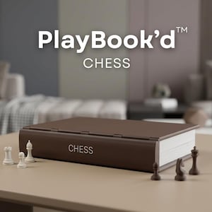 Puede incluir: Un juego de ajedrez marrón con el texto "PlayBook'd CHESS" sobre una mesa. El juego de ajedrez tiene forma de libro, con la palabra "CHESS" impresa en el lateral. Las piezas de ajedrez blancas y marrones están dispuestas alrededor del libro.
