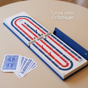 May include: A cribbage board game with a blue, red, and white design, and a deck of playing cards. The board is open, showing the track for the pegs. The text "Turns into Cribbage" is visible.