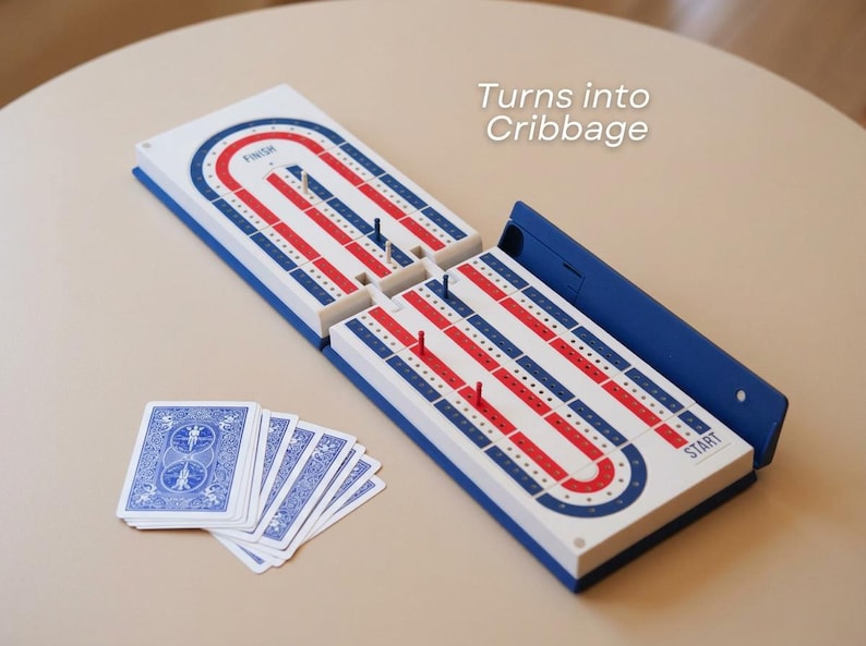 May include: A cribbage board game with a blue, red, and white design, and a deck of playing cards. The board is open, showing the track for the pegs. The text "Turns into Cribbage" is visible.