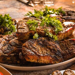 May include: A close-up shot of grilled meat on a white plate, garnished with fresh parsley. The meat is a deep brown color with visible grill marks, suggesting it's been cooked to perfection. The image evokes a sense of a delicious meal.