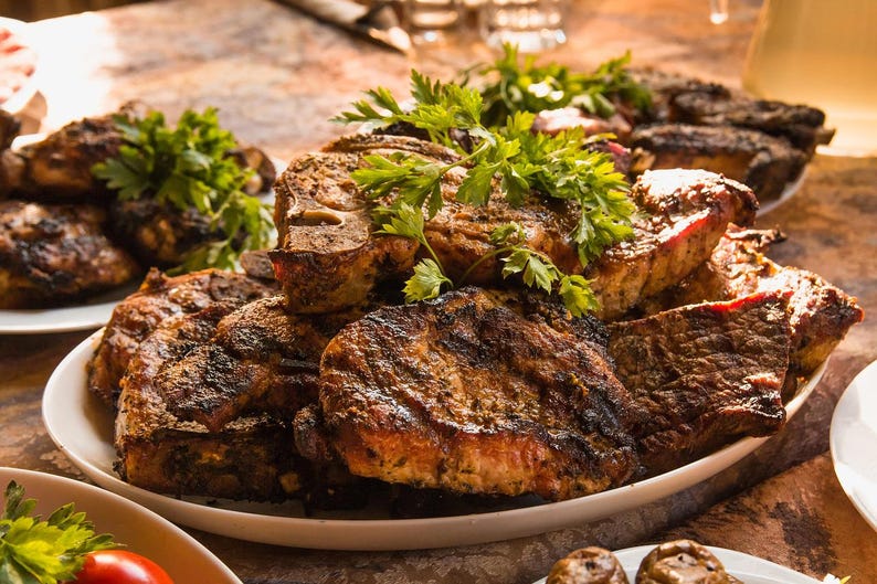 May include: A close-up shot of grilled meat on a white plate, garnished with fresh parsley. The meat is a deep brown color with visible grill marks, suggesting it's been cooked to perfection. The image evokes a sense of a delicious meal.