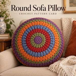 May include: A round crochet pillow featuring concentric rings of purple, olive green, red, blue, and orange yarn in a textured stitch pattern. The text "Round Sofa Pillow CROCHET PATTERN CARD" is printed in black above the pillow.