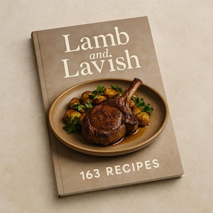 Pode incluir: Um livro de receitas intitulado "Lamb and Lavish" com o texto "163 RECIPES" na capa. Um prato de costeletas de cordeiro e batatas cozidas com salsa está em cima do livro. A capa do livro é de cor castanho claro.