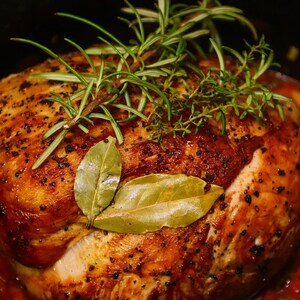 May include: A roasted turkey breast, golden brown with herbs, bay leaves, and rosemary sprigs. The turkey sits in a bed of cooked vegetables, creating a delicious and appetizing meal. A close-up shot of a home-cooked dish.
