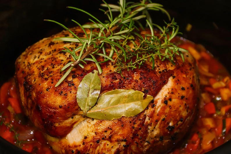 May include: A roasted turkey breast, golden brown with herbs, bay leaves, and rosemary sprigs. The turkey sits in a bed of cooked vegetables, creating a delicious and appetizing meal. A close-up shot of a home-cooked dish.