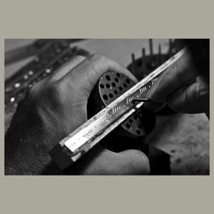 May include: A person's hand holding a metal tool with a ruler and a series of small holes. The tool is being used to mark a piece of metal.