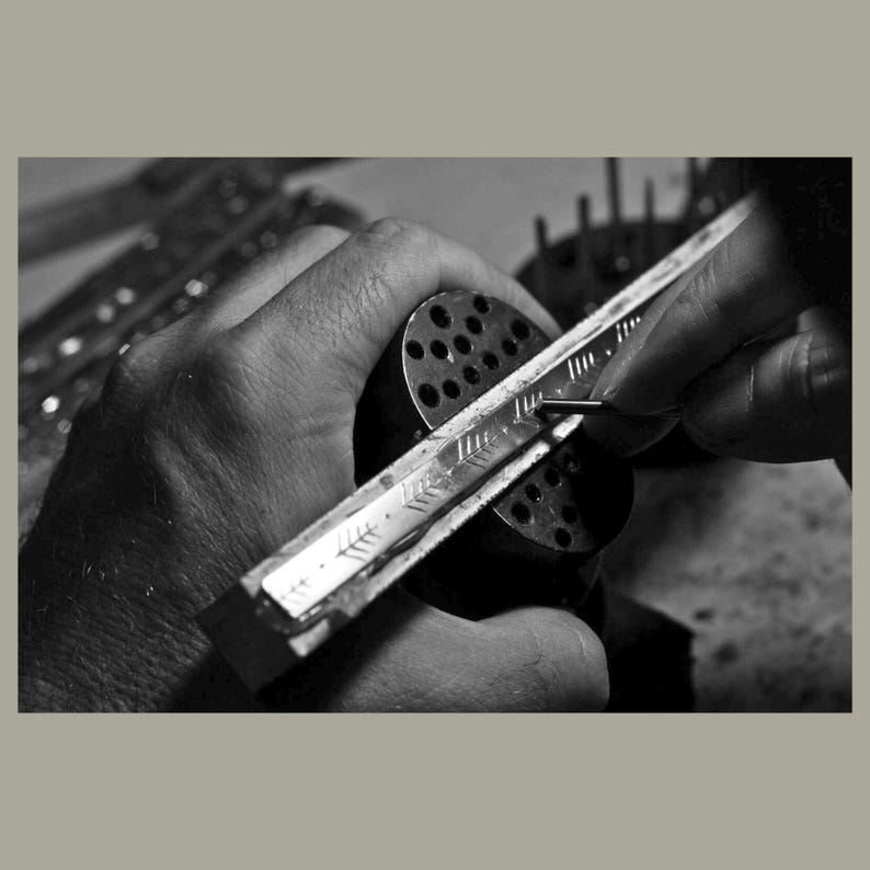 May include: A person's hand holding a metal tool with a ruler and a series of small holes. The tool is being used to mark a piece of metal.