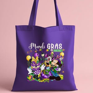 K&ouml;nnte beinhalten: Lila Tragetasche mit einem Mardi Gras-Design. Die Grafik zeigt Minnie und Mickey Mouse in Karnevalskost&uuml;men, die Worte "Mardi Gras" in wei&szlig;er Schrift und ein "Main Street"-Schild. Gelbe Luftballons und Konfetti erg&auml;nzen die festliche Szene.