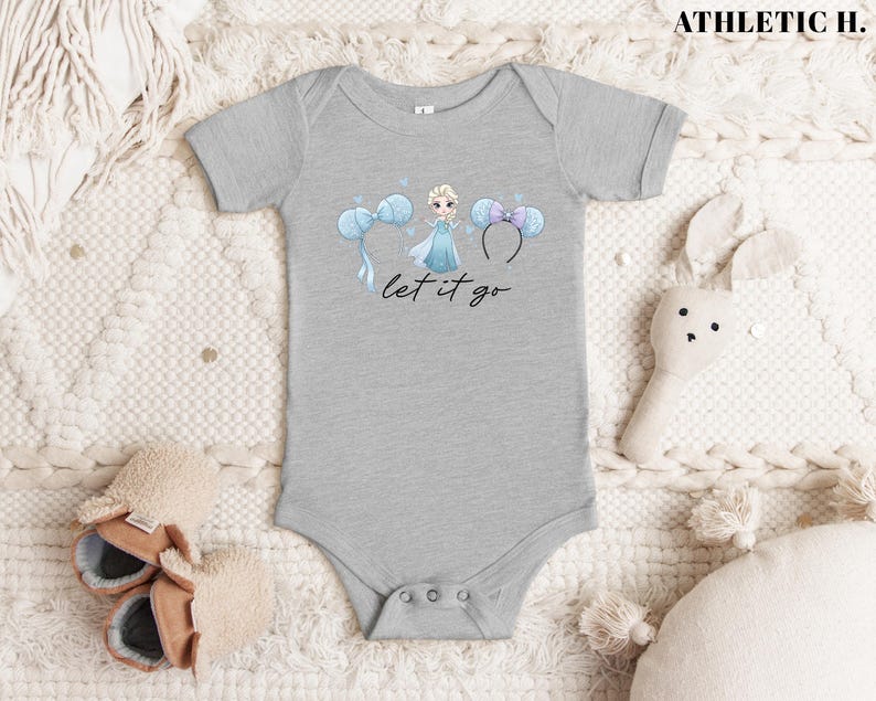 K&ouml;nnte beinhalten: Ein grauer Baby-Body mit einer Cartoon-Illustration einer Prinzessin in einem blauen Kleid, mit blauen und lila Micky-Maus-Ohren und dem Text "let it go". In der oberen rechten Ecke steht der Text "ATHLETIC H."