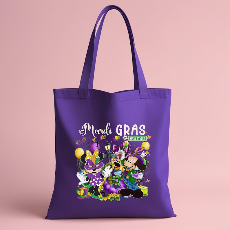 K&ouml;nnte beinhalten: Lila Tragetasche mit einem Mardi Gras-Design. Die Grafik zeigt Minnie und Mickey Mouse in Karnevalskost&uuml;men, die Worte "Mardi Gras" in wei&szlig;er Schrift und ein "Main Street"-Schild. Gelbe Luftballons und Konfetti erg&auml;nzen die festliche Szene.
