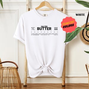May include: White t-shirt with the text "Salted Butter" and a nutrition label graphic. The text "Comfort Colors" is on a pink circle.