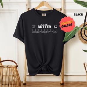 May include: Black t-shirt with white text that reads "Salted Butter Grade AA" and a chart with different measurements of butter. The shirt has a knotted design in the front.
