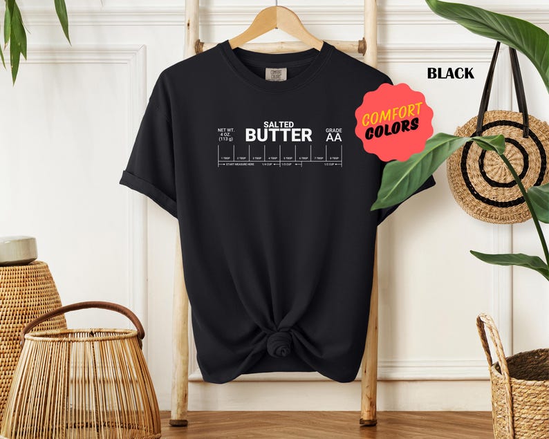 May include: Black t-shirt with white text that reads "Salted Butter Grade AA" and a chart with different measurements of butter. The shirt has a knotted design in the front.
