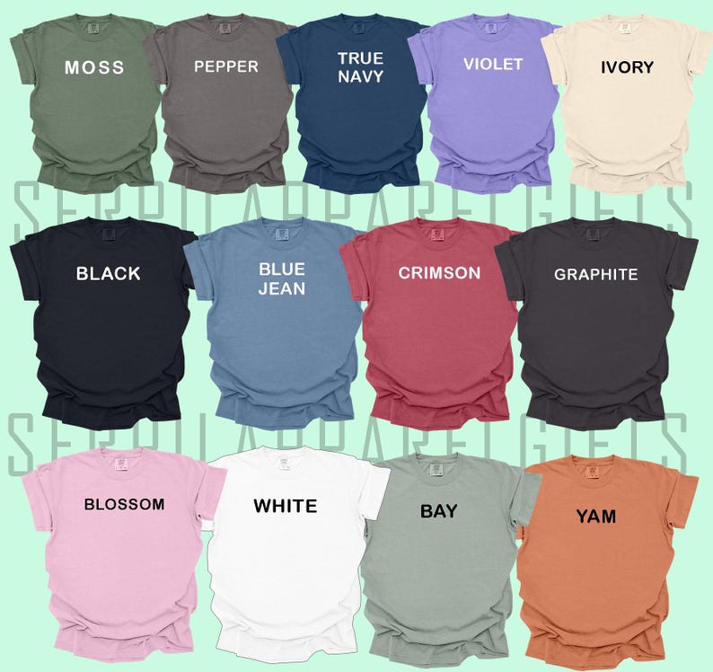 May include: A collection of 14 t-shirts in various colours, including moss green, pepper, true navy, violet, ivory, black, blue jean, crimson, graphite, blossom, white, bay, and yam. Each shirt has a different colour and a single word printed on the front.