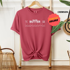 May include: A crimson t-shirt with the text "SALTED BUTTER" and a chart showing different grades of butter. The text "COMFORT COLORS" is in a yellow speech bubble.