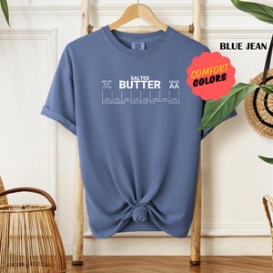 May include: A blue jean t-shirt with white text that reads "Salted Butter" and a chart with the words "Net Wt 1/2 oz (17.5 g)" and "Grade AA". The shirt has a comfort colours tag.