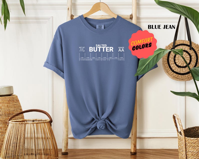 May include: A blue jean t-shirt with white text that reads "Salted Butter" and a chart with the words "Net Wt 1/2 oz (17.5 g)" and "Grade AA". The shirt has a comfort colours tag.