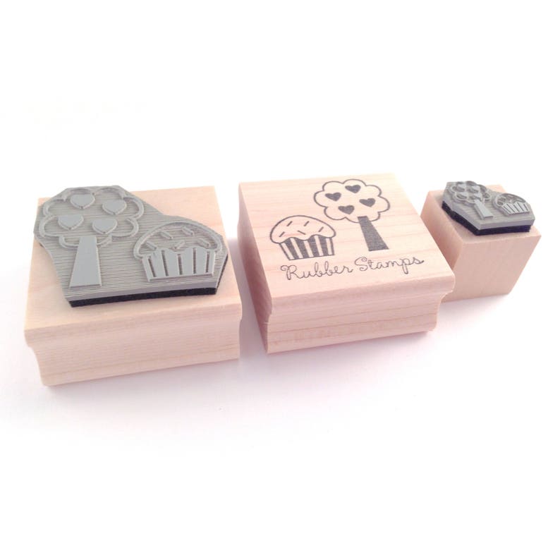 May include: Three wooden mounted rubber stamps with images of a cupcake and a tree with hearts. The stamps are labeled "Rubber Stamps".