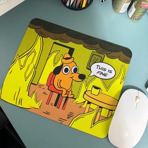 May include: A yellow mouse mat featuring a cartoon dog sitting in a chair in a burning house. The dog has large eyes and is wearing a hat. The text "This is FINE" is in a speech bubble above the dog.