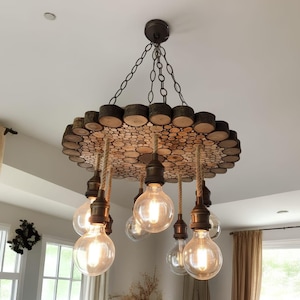 Può includere: Lampadario rustico in legno dal design circolare, caratterizzato da una moltitudine di piccole fette di legno. L'apparecchio ha diverse lampadine in stile Edison sospese con corde. L'apparecchio è fissato al soffitto con una catena.