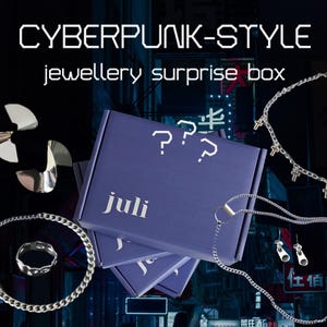 Op de afbeelding: Een paarse cyberpunk-stijl sieraden verrassingsdoos met de naam "juli" en vraagtekens. Zilveren sieraden, waaronder een ring, oorbellen en kettingen, worden rond de doos getoond. De tekst "CYBERPUNK-STYLE jewellery surprise box" staat bovenaan.