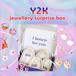 Könnte beinhalten: Y2K-Schmuck-Überraschungsbox mit Ringen, Halsketten, Ohrringen und einer Perlenkette. Die Box enthält kleine Kordelzugbeutel mit dem Aufdruck "juli". Die Box trägt den Text "Chosen for you".
