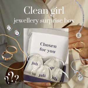 Könnte beinhalten: Eine Schmuck-Überraschungsbox mit dem Text "Clean girl jewellery surprise box". Die Box enthält kleine weiße Beutel mit dem Aufdruck "juli". Das Bild zeigt auch Ringe, Ohrringe und eine Halskette mit dem Buchstaben "E".