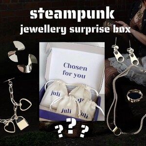 May include: A steampunk jewelry surprise box with various silver-toned jewelry pieces. The box contains small drawstring bags with the name "juli" on them. The text "Chosen for you" is visible inside the box. Other jewelry includes earrings, a necklace, and a ring.