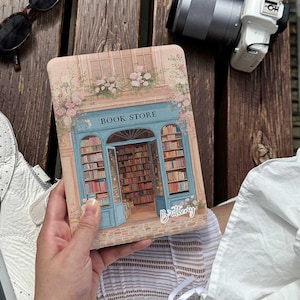 Op de afbeelding: Rechthoekige hoes met een gedetailleerde illustratie van een boekhandelfaçade. Het ontwerp omvat een blauwe deur, boekenplanken en de tekst "BOOK STORE" erboven. Bloemenaccenten en de naam "Brittany" zijn ook zichtbaar.