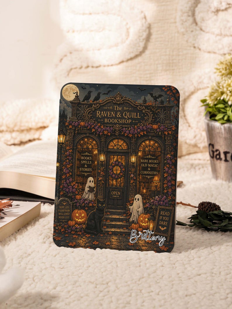 May include: A rectangular sign featuring an illustration of The Raven & Quill Bookshop with a black cat, two ghosts, pumpkins, and autumn leaves. The text reads The Raven & Quill Bookshop, Books Spells & Stories, Rare Books Old Magic & Curiosities, Open, Here Lies A Good Book Well Loved Never Lost, Read If You Dare, and Brittney.