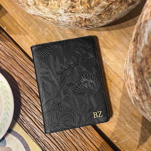 May include: Black leather passport holder with a floral embossed design and the initials "BZ" in gold lettering.
