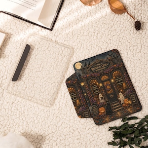 May include: A clear protective tablet case featuring a detailed illustration of The Raven & Quill Bookshop, complete with ghosts, pumpkins, a black cat, and glowing lanterns. The design includes text reading The Raven & Quill Bookshop.