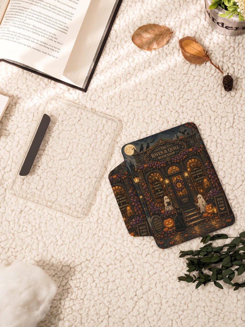 May include: A clear protective tablet case featuring a detailed illustration of The Raven & Quill Bookshop, complete with ghosts, pumpkins, a black cat, and glowing lanterns. The design includes text reading The Raven & Quill Bookshop.