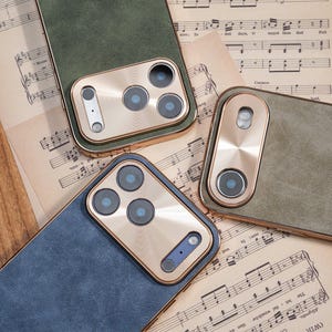 Op de afbeelding: Close-up van verschillende telefoonhoesjes in groen en blauw, met goudkleurige camerakaders. De hoesjes zijn gerangschikt op een achtergrond van vintage bladmuziek, wat een klassieke esthetiek laat zien. De hoesjes hebben een getextureerde uitstraling.