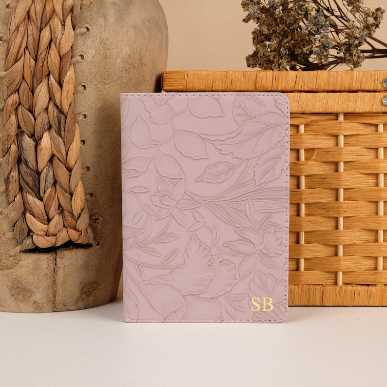 May include: A pale pink leather journal with a floral embossed design and the initials "SB" in gold lettering.