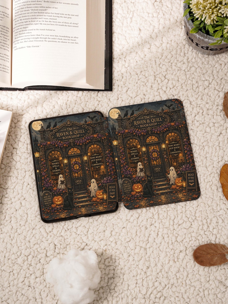 May include: Two e-readers displaying a graphic of The Raven & Quill Bookshop, featuring ghosts, a black cat, pumpkins, and autumn foliage. The shop front has signs reading Books Spells & Stories and Rare Books Old Magic & Curiosities.
