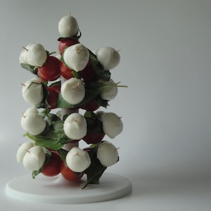 Puede incluir: Un árbol de Navidad blanco y rojo hecho de bolas de mozzarella y tomates cherry en un soporte blanco.