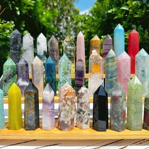 Può includere: Una collezione di 25 punte di cristallo colorate disposte su un supporto in legno. Le punte sono di varie tonalità di verde, blu, viola, rosa, giallo, rosso e nero.