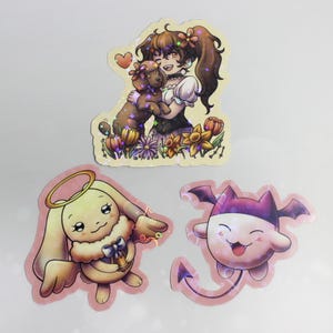May include: Three holographic stickers featuring cartoon characters. One shows a girl hugging a teddy bear in a flower garden. Another depicts a bunny with a halo. The third is a smiling devil-like creature.