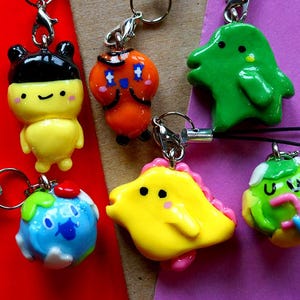 Puede incluir: Un conjunto de seis encantos de arcilla polimérica coloridos hechos a mano. Cada encanto presenta un personaje diferente con un diseño único. Los encantos están unidos a llaveros y se pueden usar como encantos de teléfono o accesorios para bolsos.