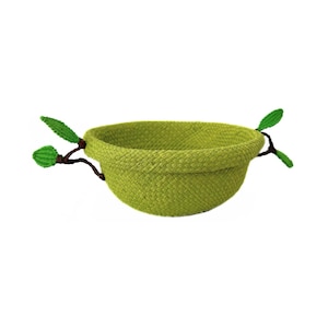 Könnte beinhalten: Eine gewebte, limettengrüne Schüssel mit abgerundeter Form. Zwei dekorative, zweigartige Elemente mit grünen Blattakzenten erstrecken sich von den Seiten. Die Schüssel steht vor einem weißen Hintergrund.